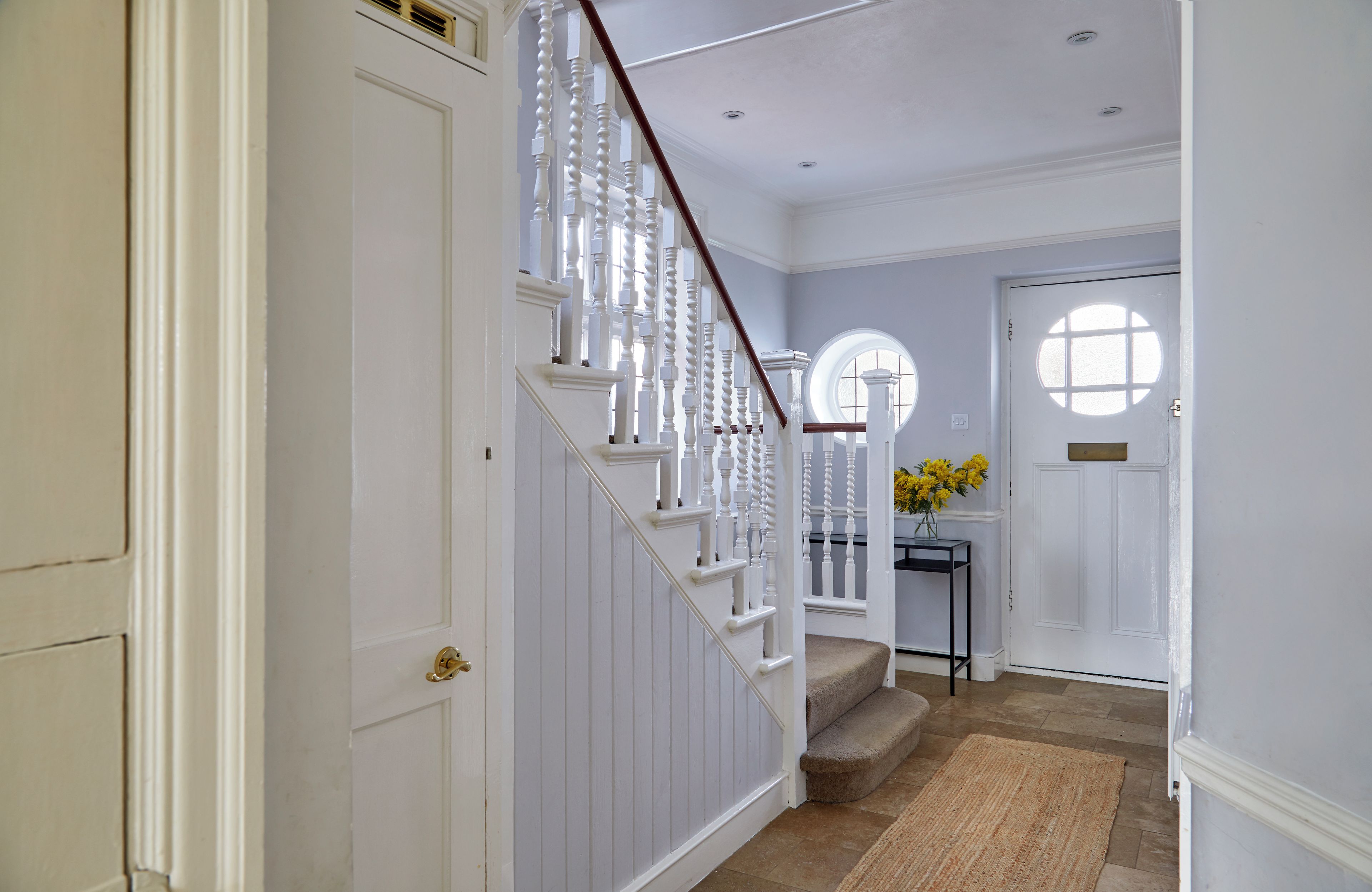 A staircase with white balusters leading to a landing, a round window, and a door with a small window.