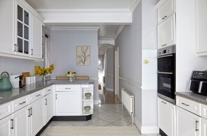 A modern kitchen with white cabinetry, a built-in oven, and a central island with a vase of flowers. - Elegant home in the heart of Wimbledon (London)