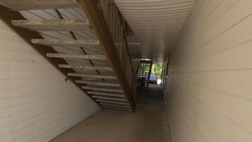 Un couloir étroit, avec un escalier en bois sur la gauche et un mur blanc sur la droite.