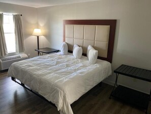 Une chambre d’hôtel avec un grand lit, une tête de lit, une table de chevet, une lampe et une fenêtre avec des rideaux.