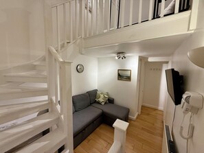 A staircase leading to a second floor, a grey sofa with cushions, a wall clock, a framed picture, and a telephone on the wall. - The Riverside Loft/En-Suite Duplex/Canada Water (London)