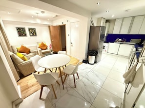 A modern kitchen with a refrigerator, stove, and sink. There is a dining area with a round table and chairs. - The Riverside Loft/En-Suite Duplex/Canada Water (London)
