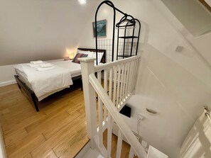 A bedroom with a bed, a bedside table, a lamp, and a white railing. - The Riverside Loft/En-Suite Duplex/Canada Water (London)