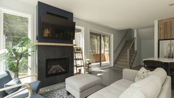 A modern living room with a fireplace, a staircase, and a kitchen area.