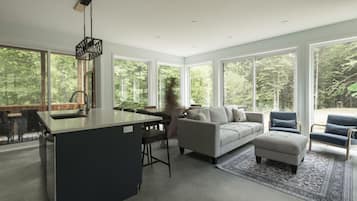 A modern interior with a kitchen island, seating area, and large windows offering a view of the forest.