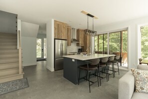 A modern kitchen with a central island, bar stools, and large windows.