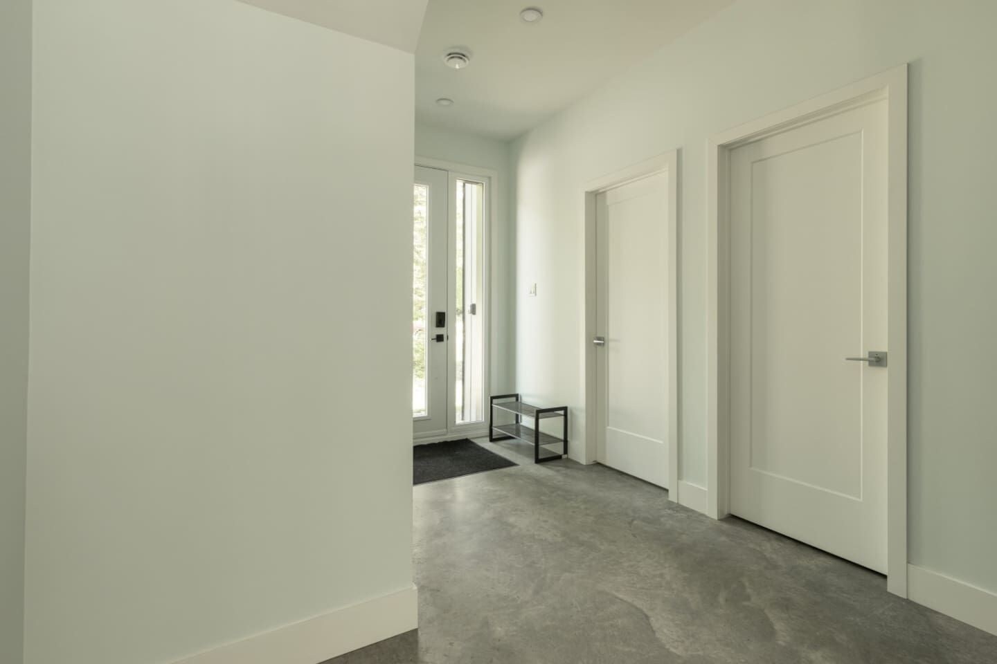 A hallway with a grey carpet, white walls, and a door at the end.