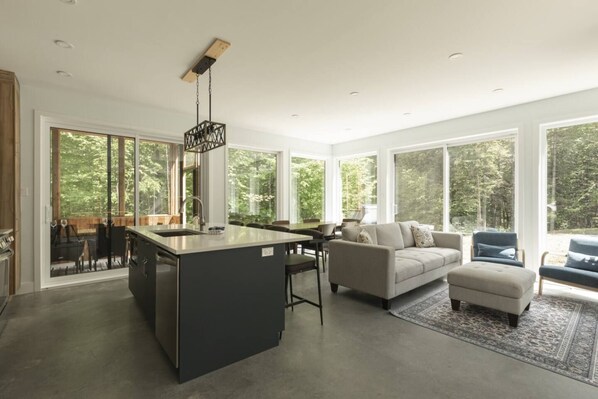 A modern interior with a kitchen island, dining area, and seating with large windows.