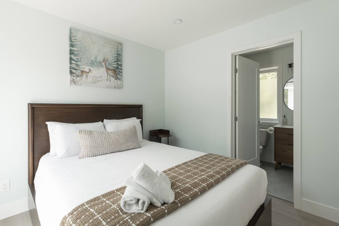 A hotel room with a large bed, a painting on the wall, and a bathroom visible through an open door.
