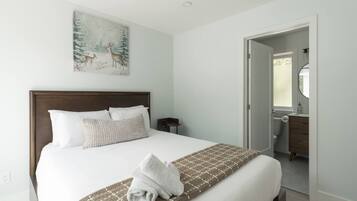 A hotel room with a large bed, a painting on the wall, and a bathroom visible through an open door.