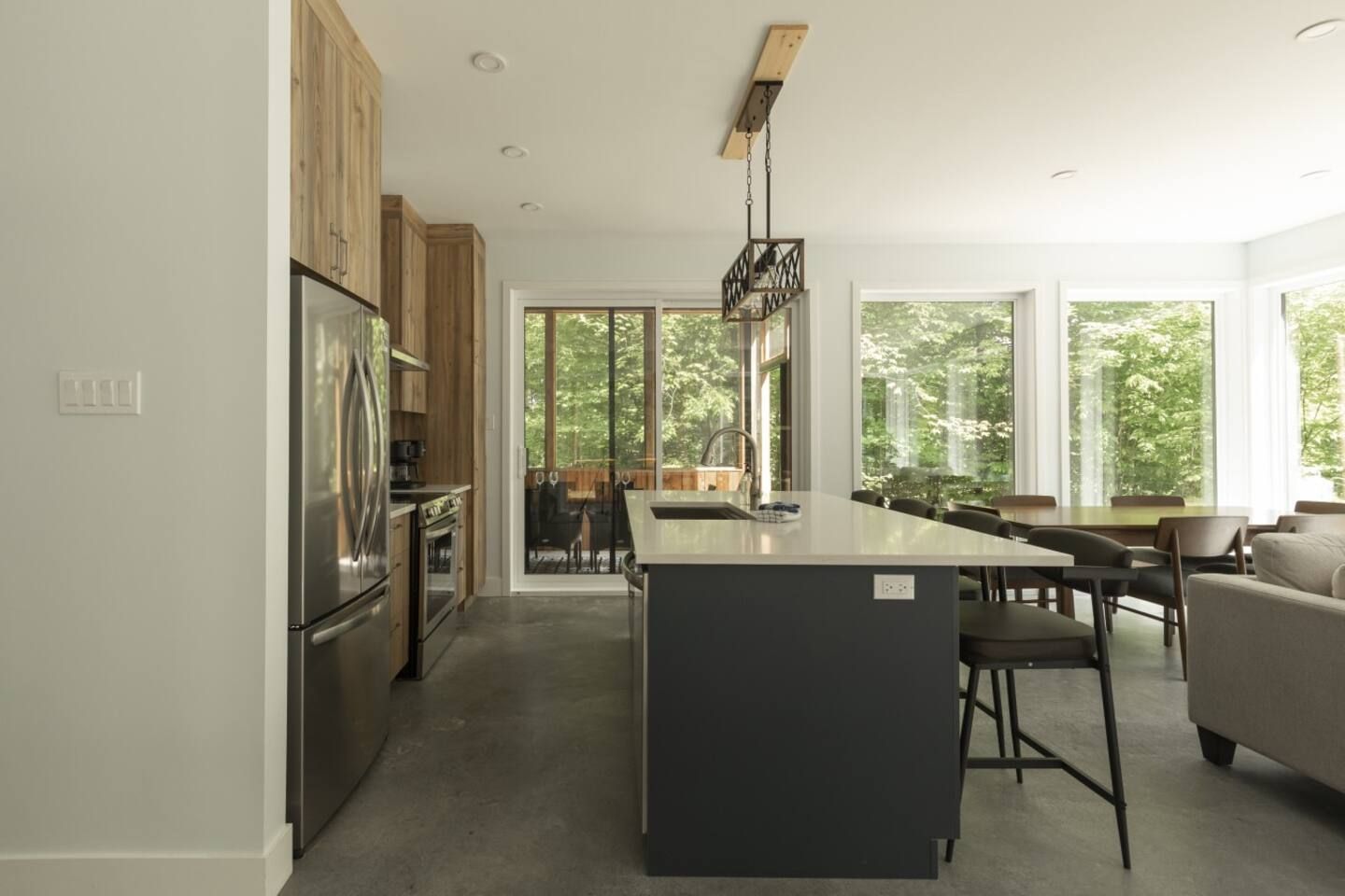 A modern kitchen with a central island, wooden cabinets, and a dining area with a sofa.