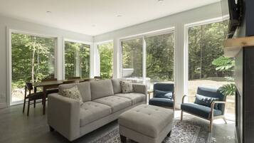A modern living room with a sectional sofa, a dining table, and a large window offering a view of the outdoors.