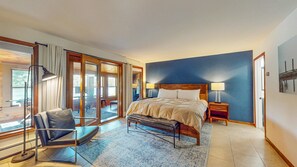 A bedroom with a large bed, a chair, a nightstand, and a view through a glass door.