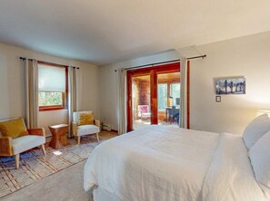 Una habitación de hotel con una cama grande, dos sillas, una mesita y vistas a través de una puerta abierta.