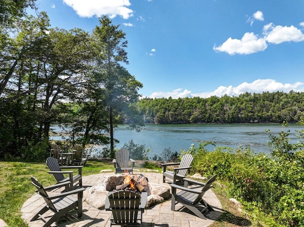 A lakeside patio with Adirondack chairs and a fire pit.