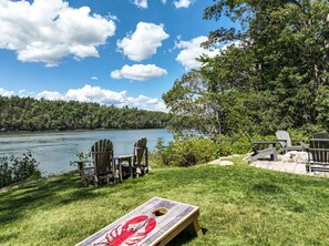 Zona de estar al aire libre frente al lago, con sillas Adirondack y una mesa de madera.