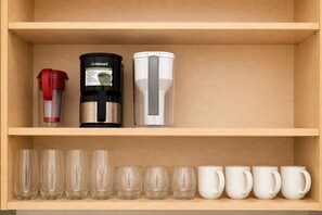 A wooden shelf with a coffee maker, a red water dispenser, and a set of clear glasses and white mugs. - 3BR Cozy and Clean House near Beach and Disney (Garden Grove)