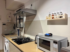 A kitchen with a gas stove, a microwave, a spice rack, and a water dispenser.