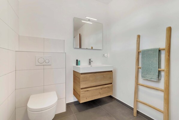 Un baño moderno con inodoro, tocador de madera con espejo y un perchero para toallas.