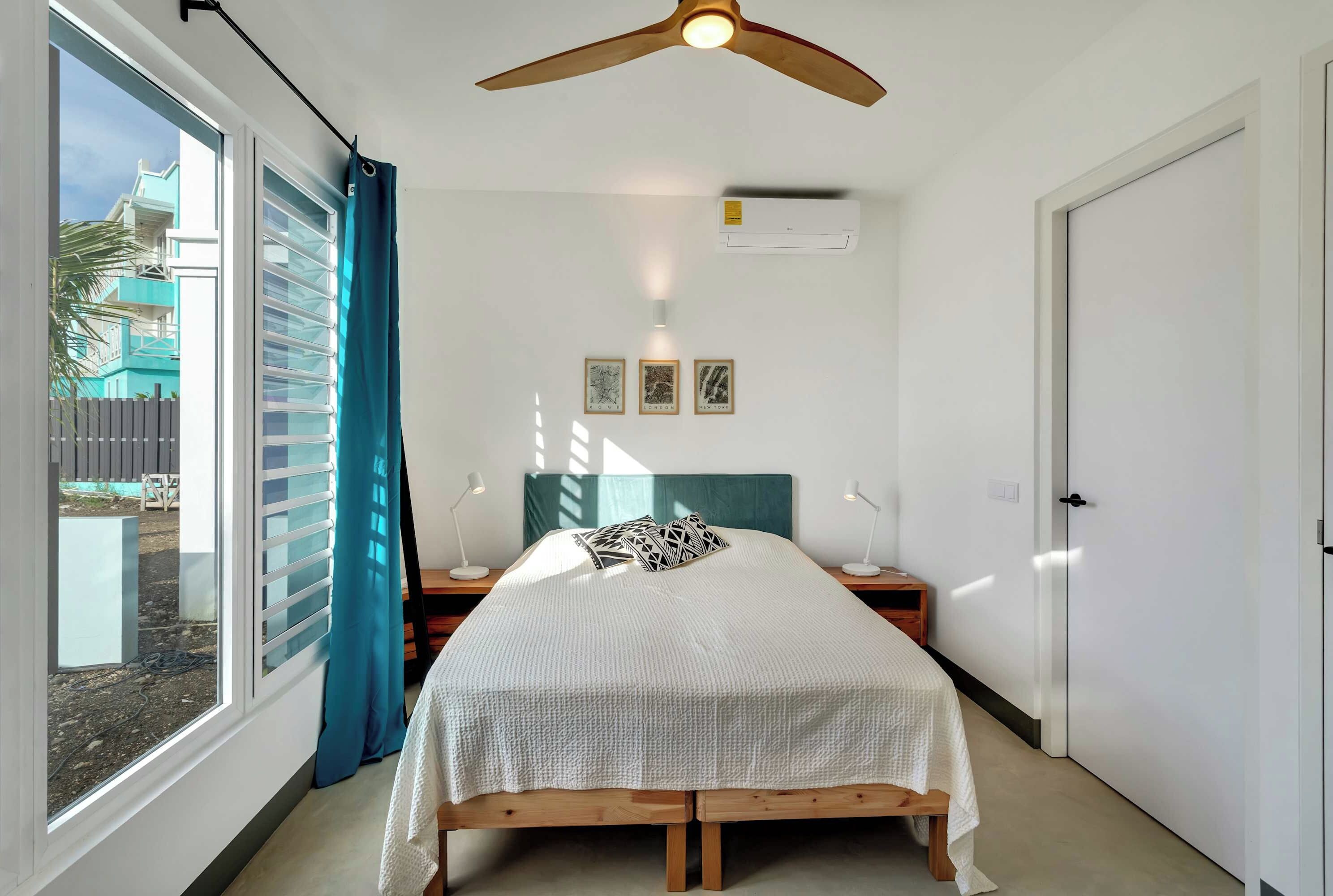 Ein Schlafzimmer mit einem Bett, Nachttischlampen, einem Deckenventilator und Blick ins Freie.