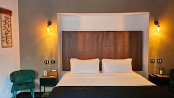 A hotel room with a large bed, two bedside lamps, a nightstand, a green chair, and a wall-mounted light fixture.