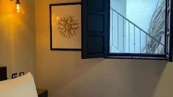 A hotel room with a bed, a wall-mounted light fixture, a framed artwork, and a window with a view of a balcony.