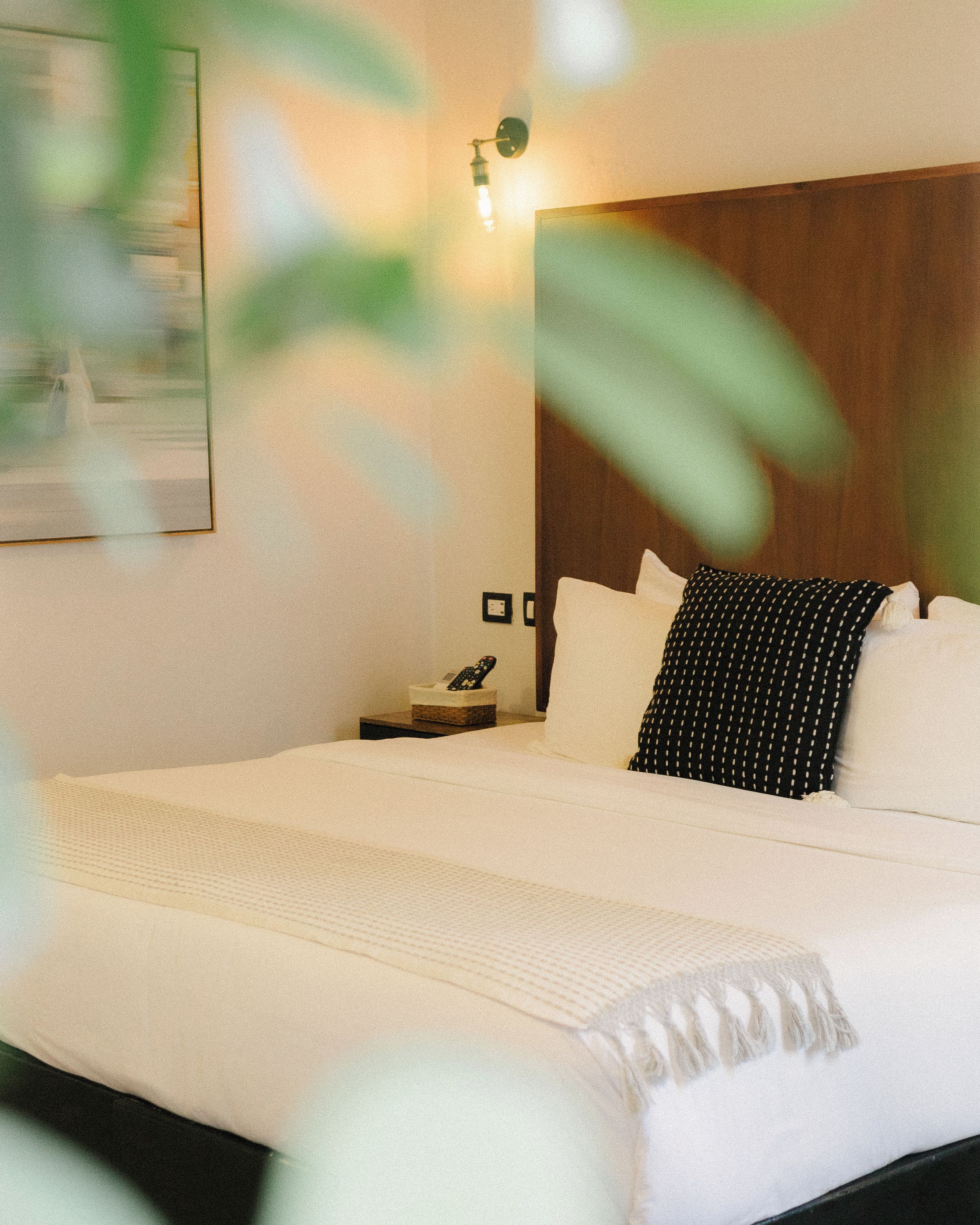 Una cama bien hecha con sábanas blancas, un cabecero de madera y una mesita de noche con una lámpara.