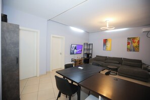Een moderne woonkamer met een donker houten tafel, een grijze bank en een flatscreen televisie die aan de muur is bevestigd.