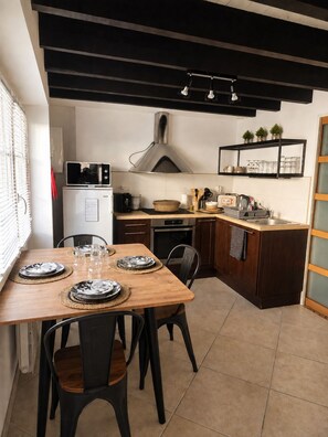 A modern kitchen with a dining area, featuring a wooden table, black chairs, a built-in oven, a microwave, and a stainless steel range hood. - PLAGE ET GARE A PIED-MAISON TYPE LOFT- (Les Sables-d'Olonne)