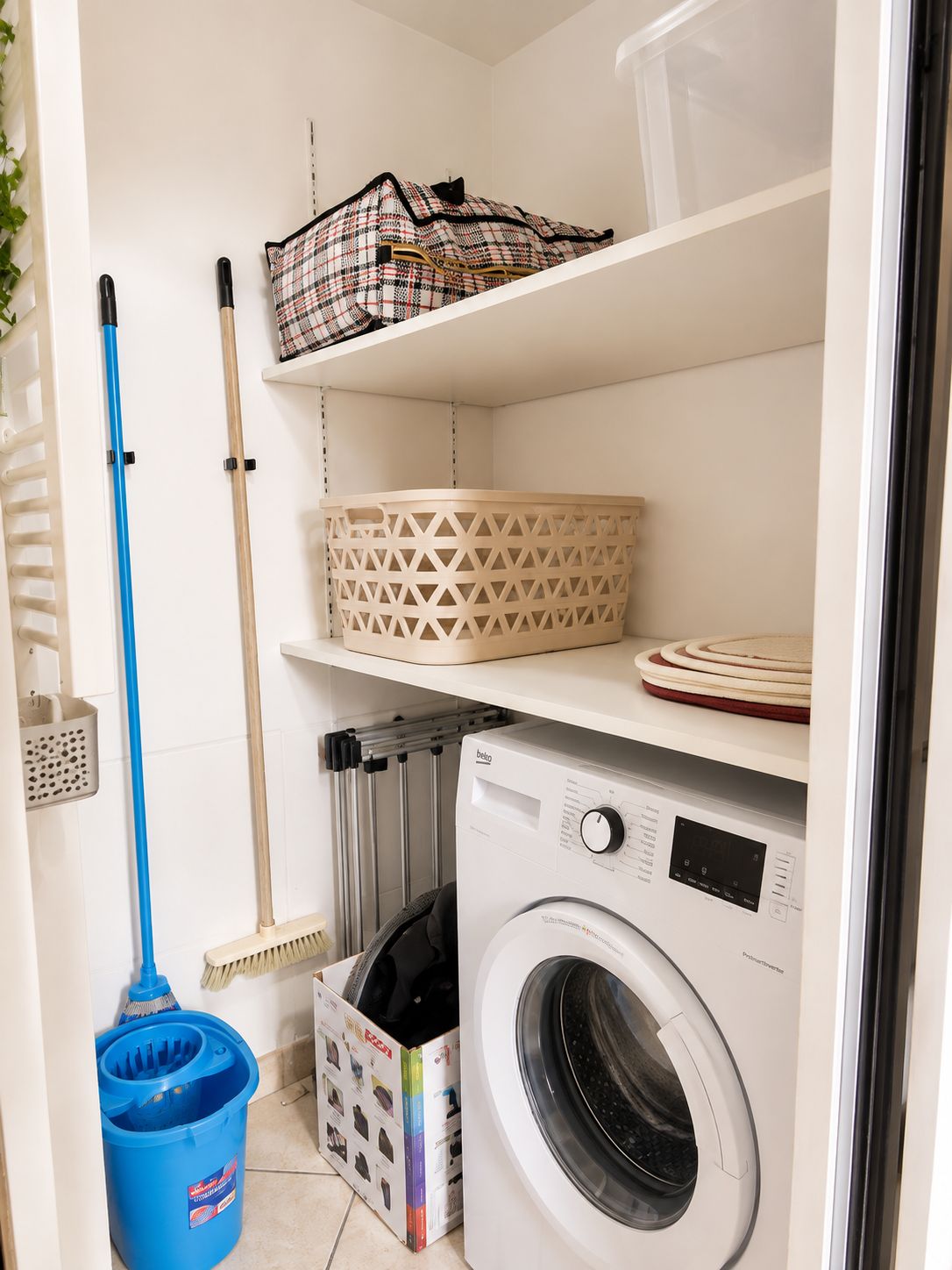 A laundry area with a washing machine, a mop, a broom, and storage baskets.