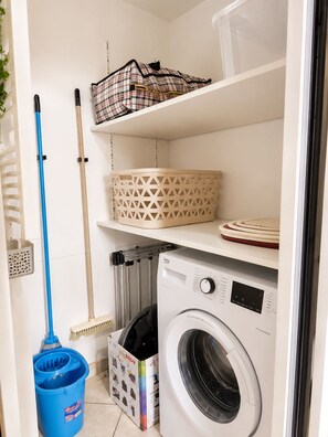 A laundry area with a washing machine, a mop, a broom, and storage baskets. - PLAGE ET GARE A PIED-MAISON TYPE LOFT- (Les Sables-d'Olonne)