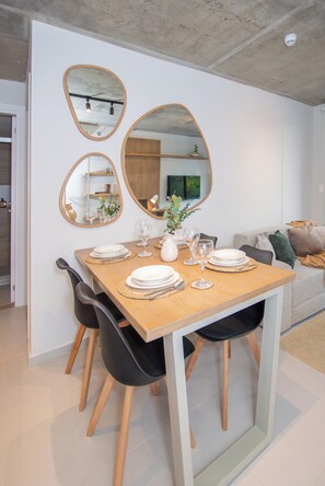 A dining area with a wooden table set for four, surrounded by black chairs. There are three wall-mounted mirrors above the table. - First del Sol 1BR | Balcony, Pool, Gym & Parking (Asunción)