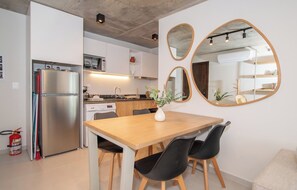 Une cuisine moderne avec un réfrigérateur en acier inoxydable, une table à manger en bois et des chaises noires, ainsi qu’un vase rempli de fleurs.