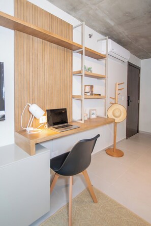 A modern office space with a wooden desk, a laptop, a white desk lamp, a black office chair, and a wall-mounted shelf unit. - First del Sol 1BR | Balcony, Pool, Gym & Parking (Asunción)
