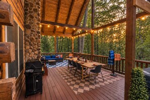 Een terras buiten met een geruit vloer, een barbecue, een eettafel met stoelen en een bank.