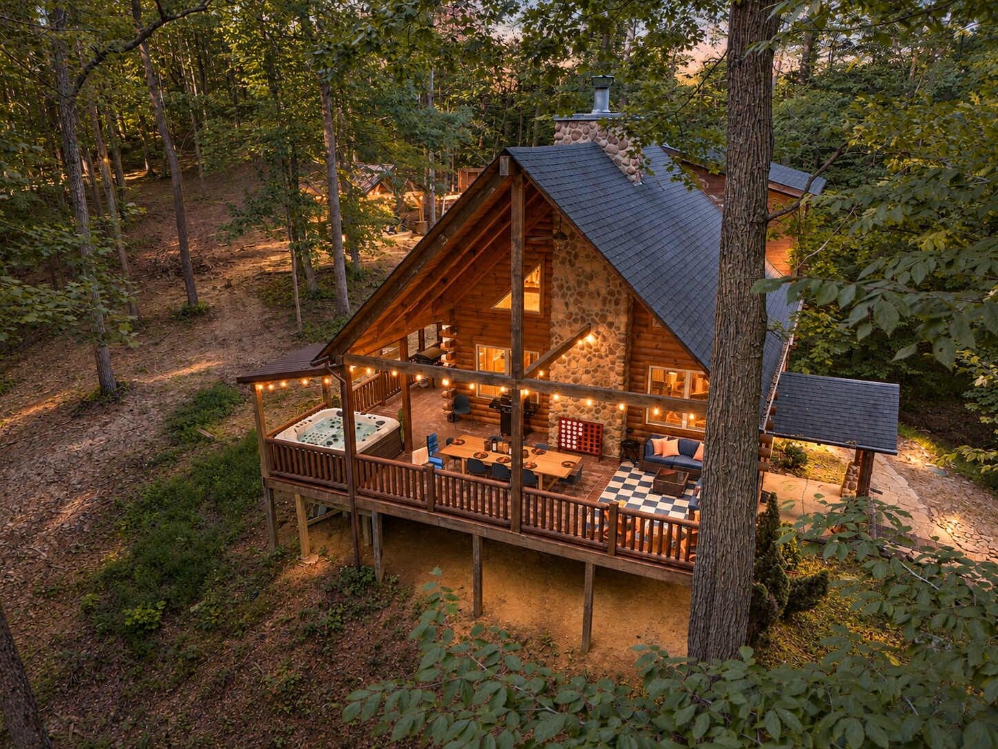 A log cabin with a deck, hot tub, and outdoor seating area surrounded by trees.