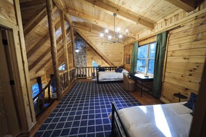 Een kamer met een hoog houten plafond en een schuine kap, met een bed, bureau en een raam met gordijnen.