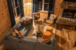 Een gezellig blokhutinterieur met een bank, fauteuils, een bijzettafeltje en een open haard.