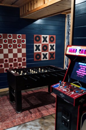 Een tafelvoetbaltafel, een damspel en een basketbal-arcadekast in een kamer met blauwe muren.