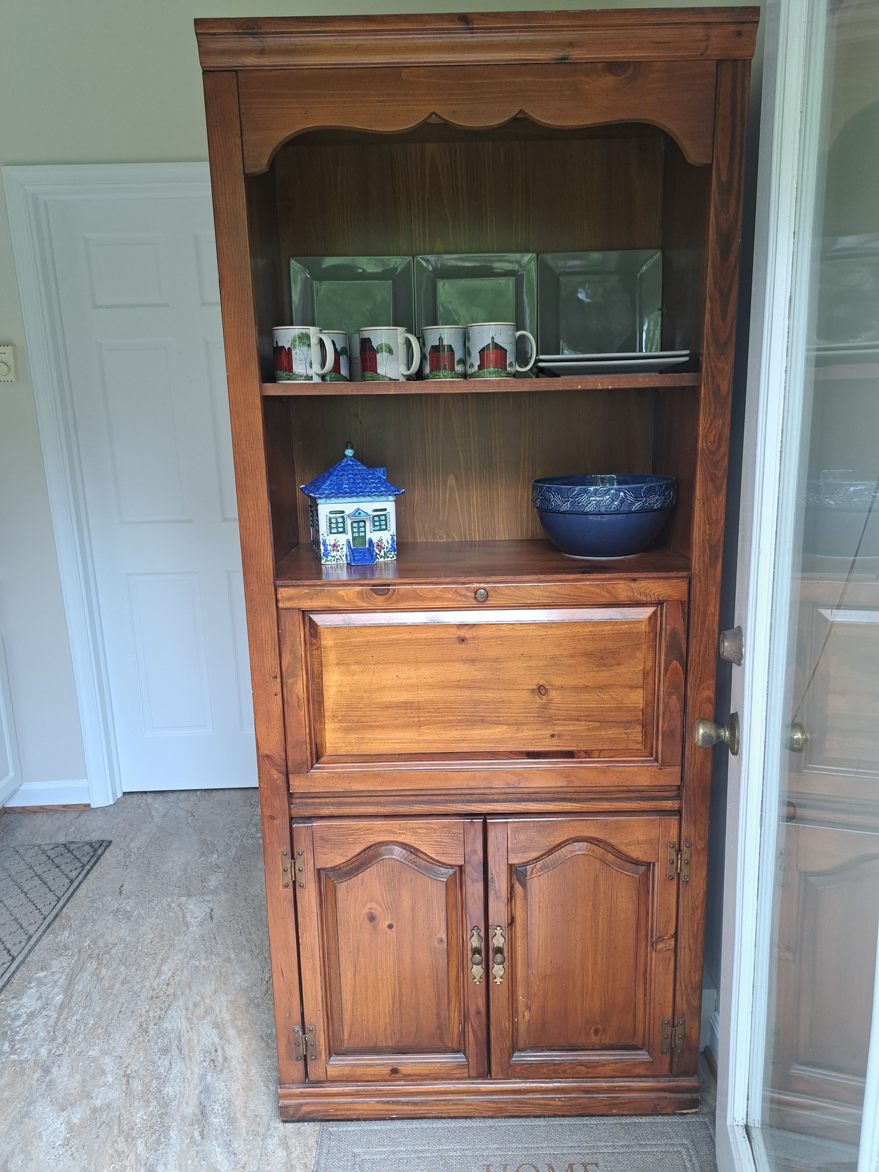 Un gabinete de madera con repisas, un tazón azul y un recipiente con forma de casa.