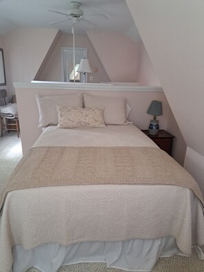Ein Schlafzimmer mit Bett, Deckenventilator, Nachttisch mit Lampe und Stuhl.