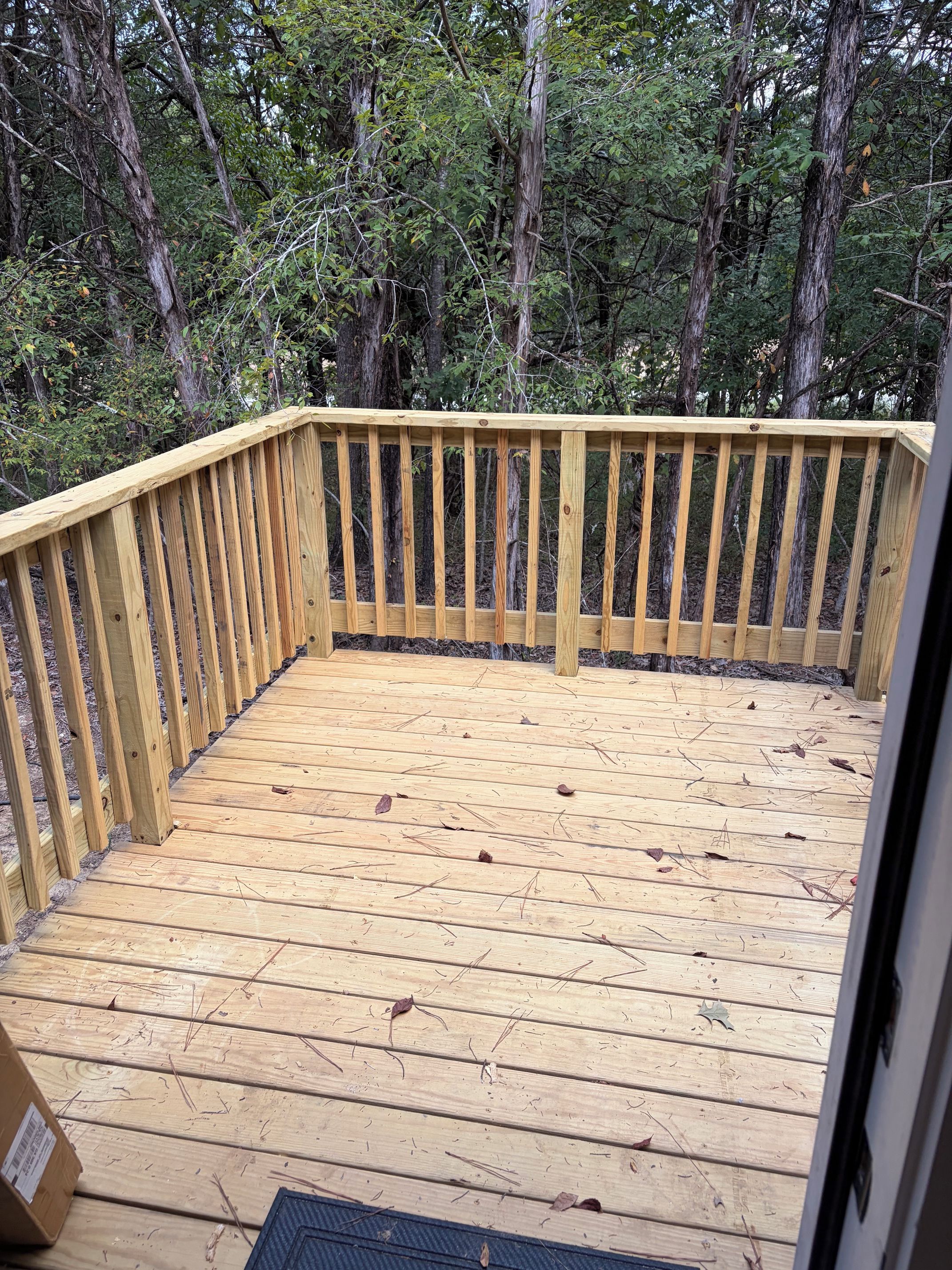 Une terrasse en bois avec une rambarde, entourée d’arbres.