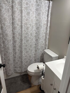 A bathroom with a toilet, a white sink, and a shower curtain with a floral pattern. - Secluded Two-Bedroom House with Bunk Nook 5 minutes from Campus. (Starkville)
