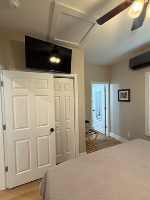 A bedroom with a bed, a television mounted above a door, and a hallway leading to another room.