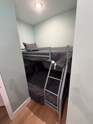 Una cama litera con escalera, un almohadón y una pared de color claro.