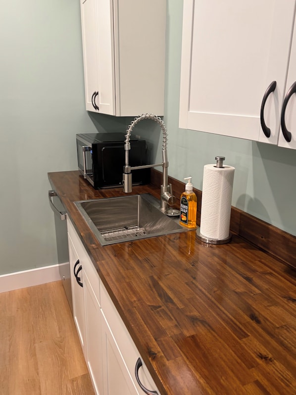 Una cocina con un lavamanos de acero inoxidable, un microondas negro y una botella de jabón para manos en la encimera.
