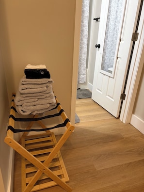 A wooden drying rack with folded towels and a black bag against a beige wall.