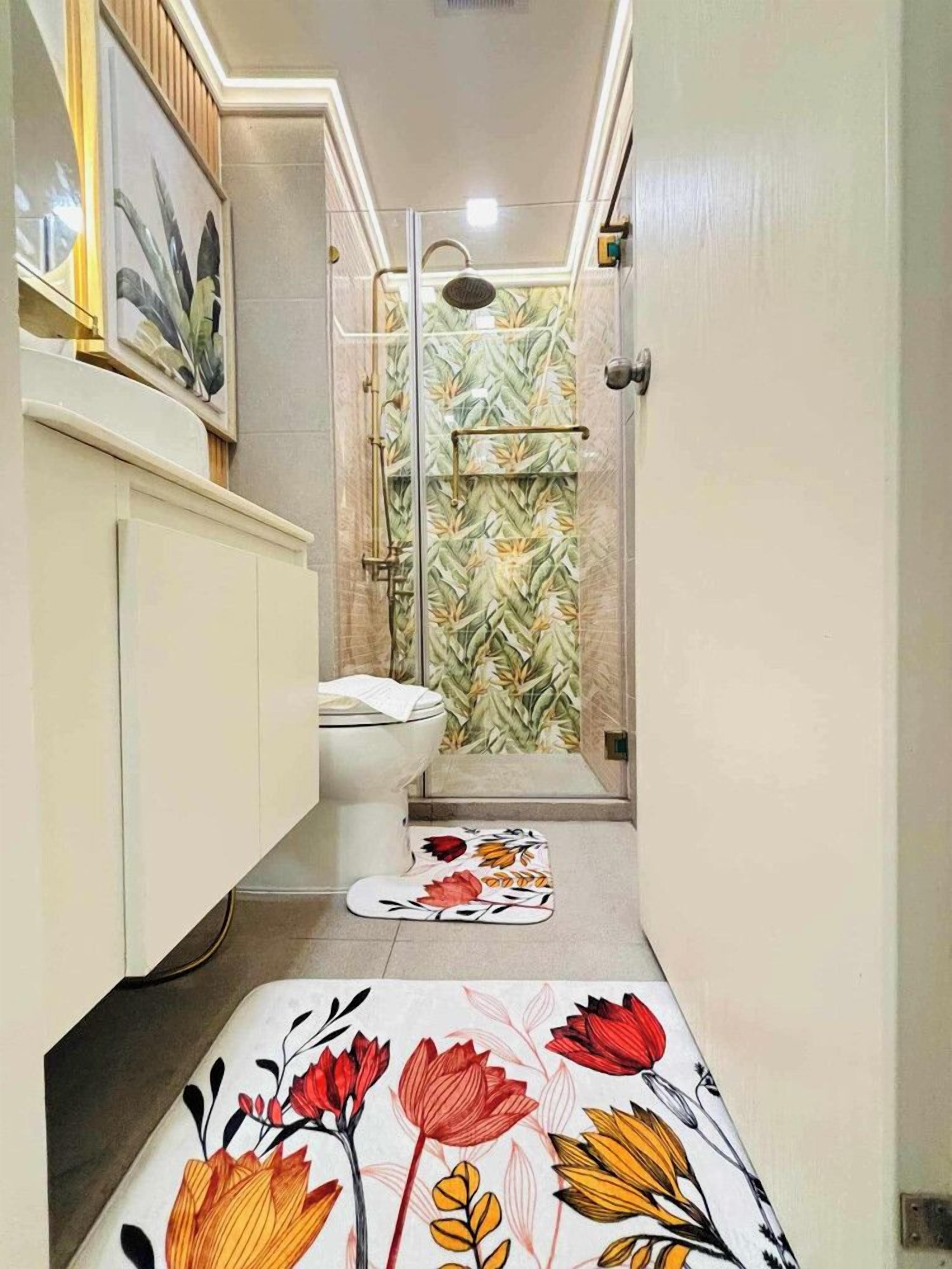 A narrow bathroom with a shower, toilet, and a decorative rug.