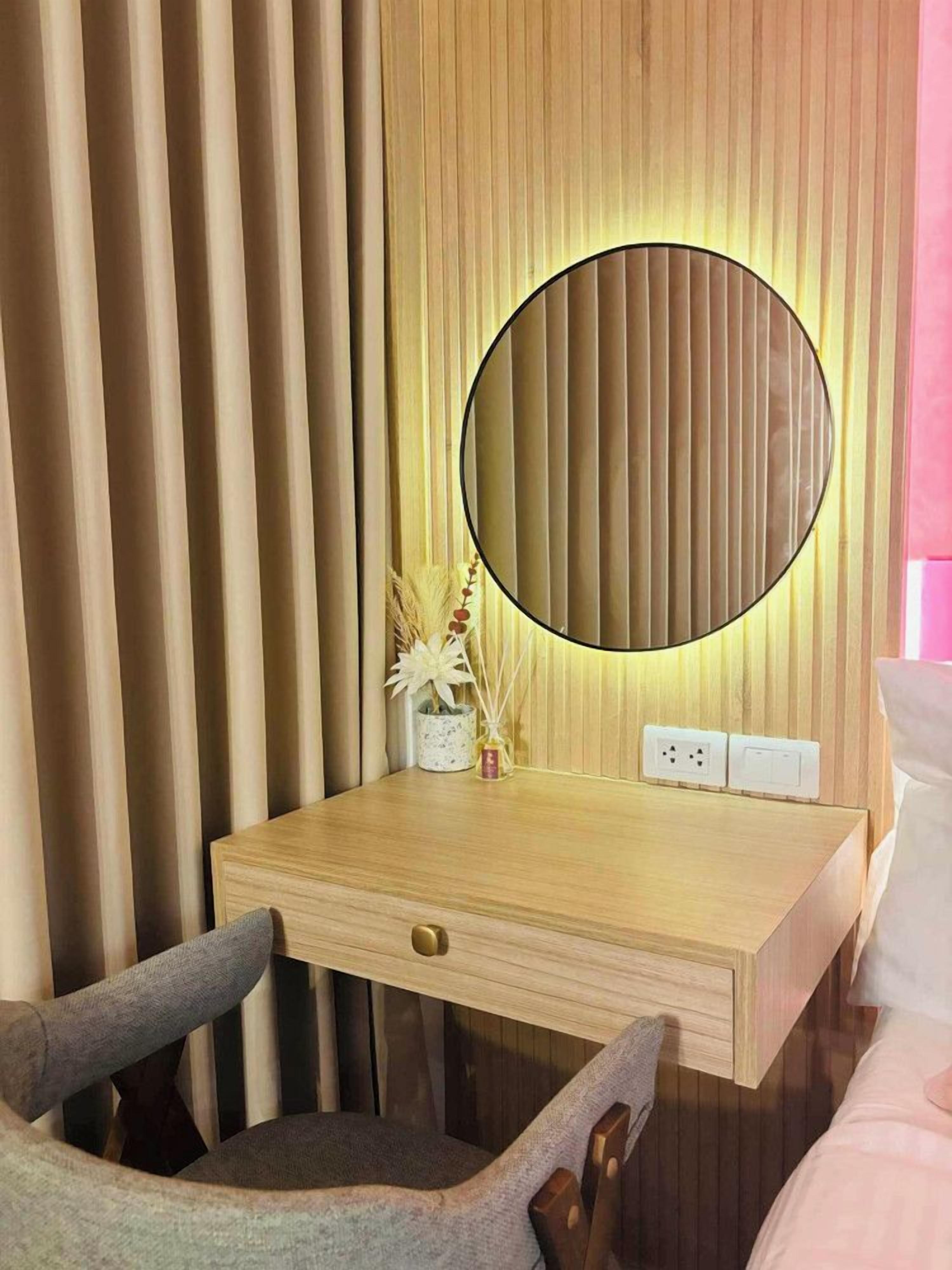 A wooden desk with a round mirror, a small vase with dried plants, and a power outlet.