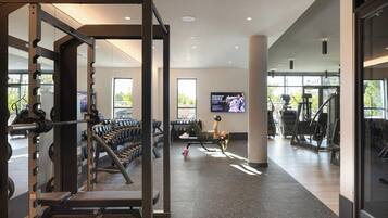 A modern gym with weightlifting equipment, cardio machines, and a TV screen.